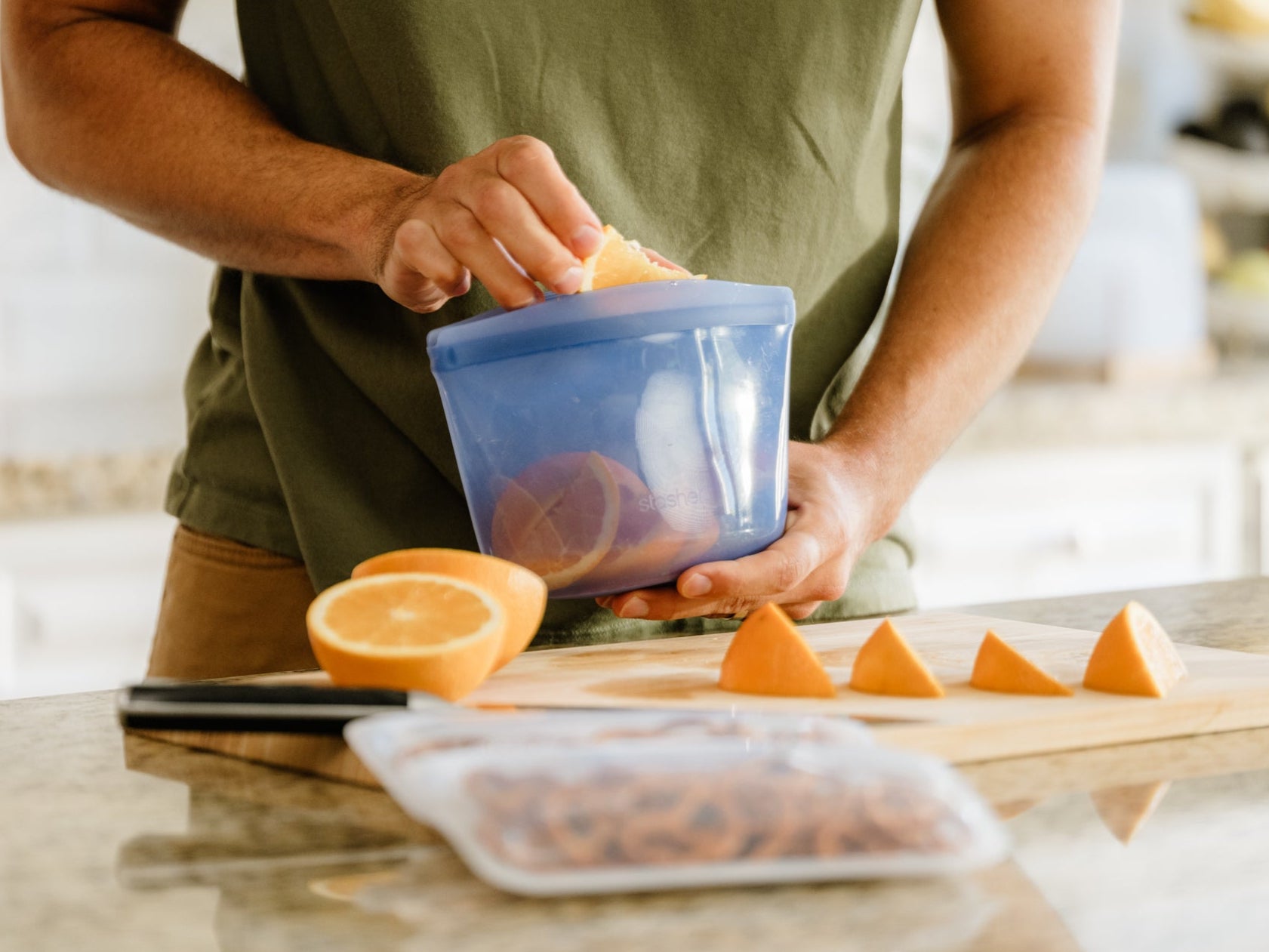 shop stasher and live life with less plastic. Image of a man filling a Stasher 2-Cup Bowl with orange slices in a kitchen. 