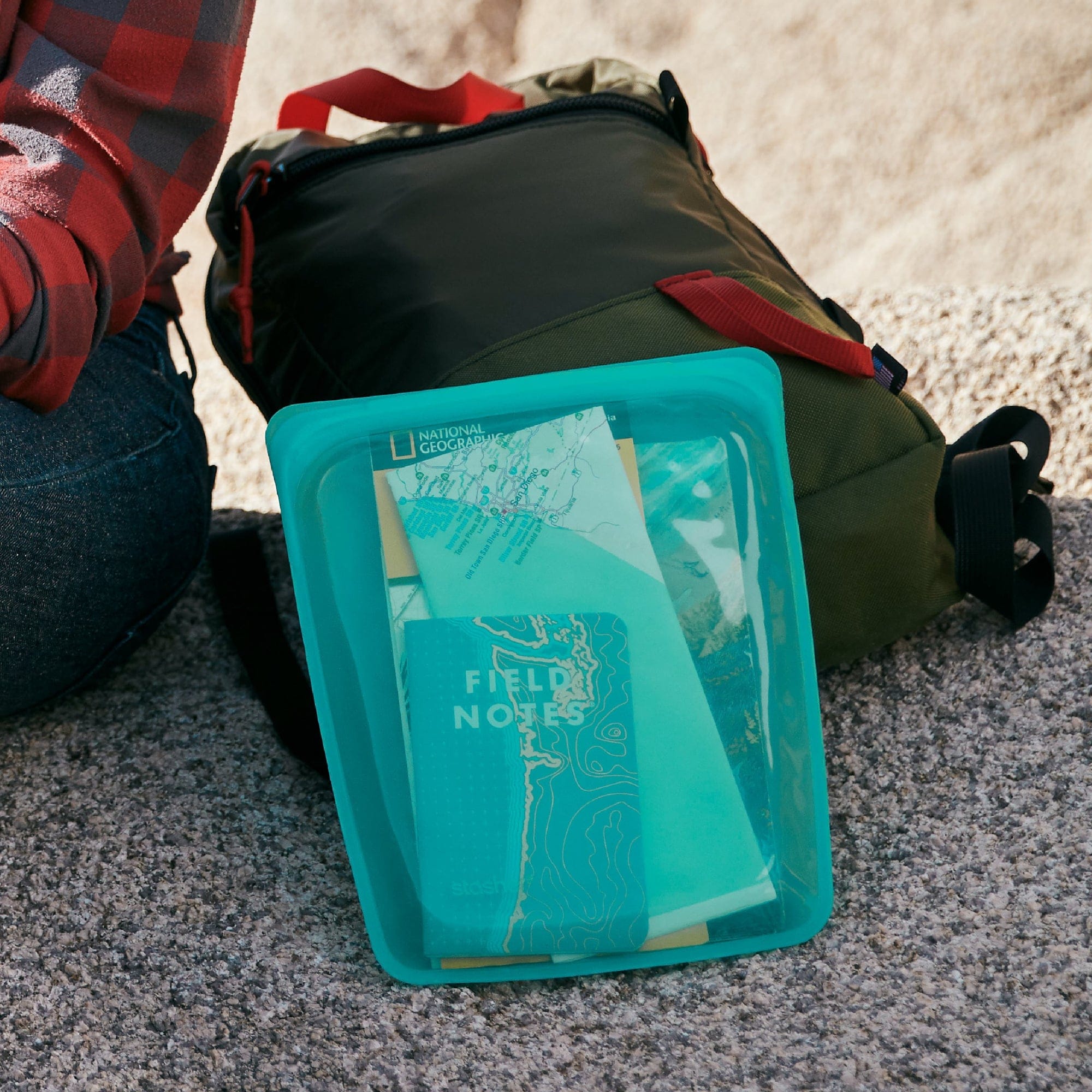 aqua: half gallon bag in aqua holding field notes and maps leaning up against a backpack. 