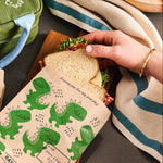 dinosaur: sandwich paper bag holding a sandwich over a table scape. 