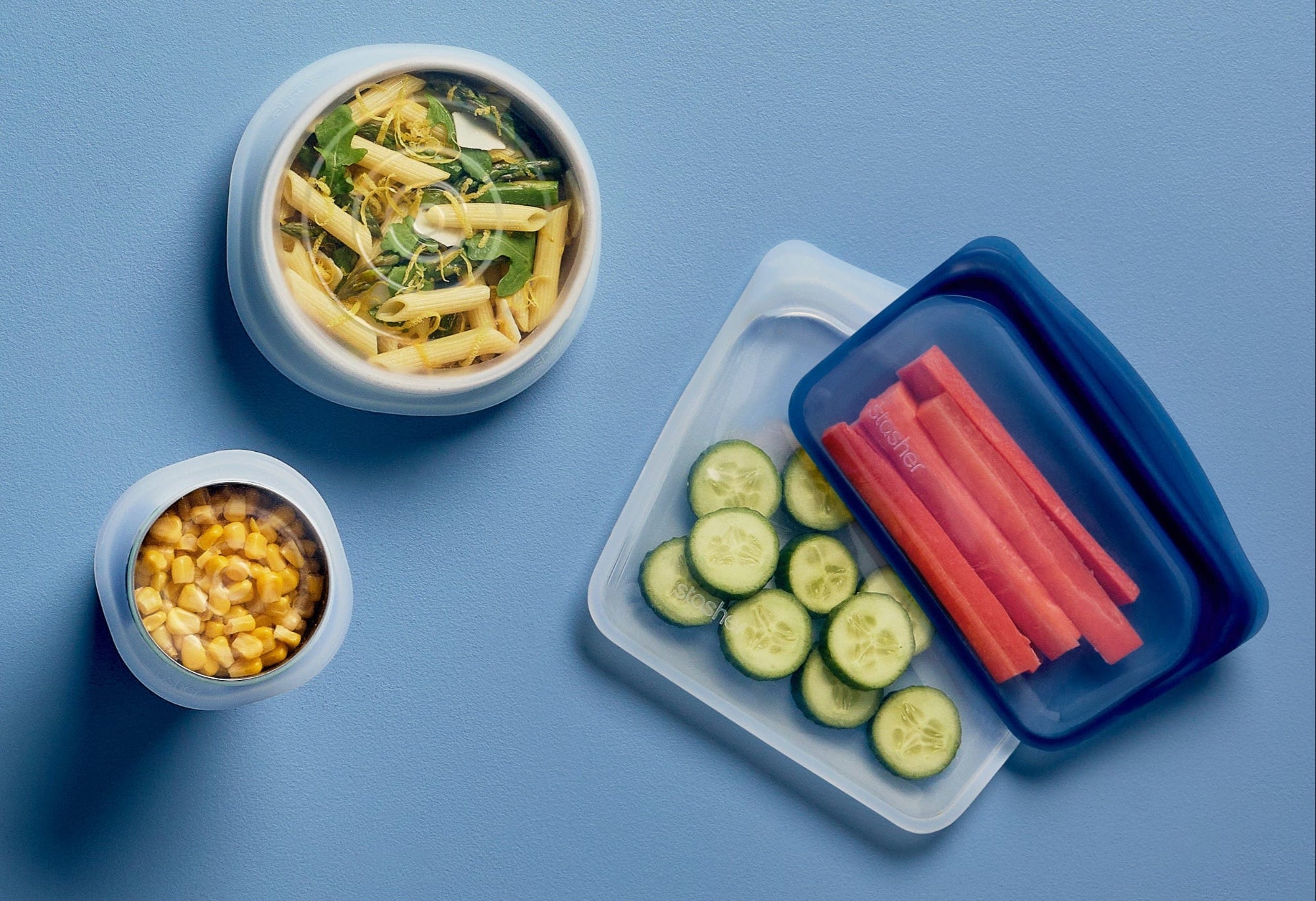 life with less plastic, shop stasher and replace 100s of single-use plastic bags. Image of 2 bowls holding pasta and corn covered by Stasher stretch lids, and a snack and sandwich stasher holding cut carrots and cucumber. 