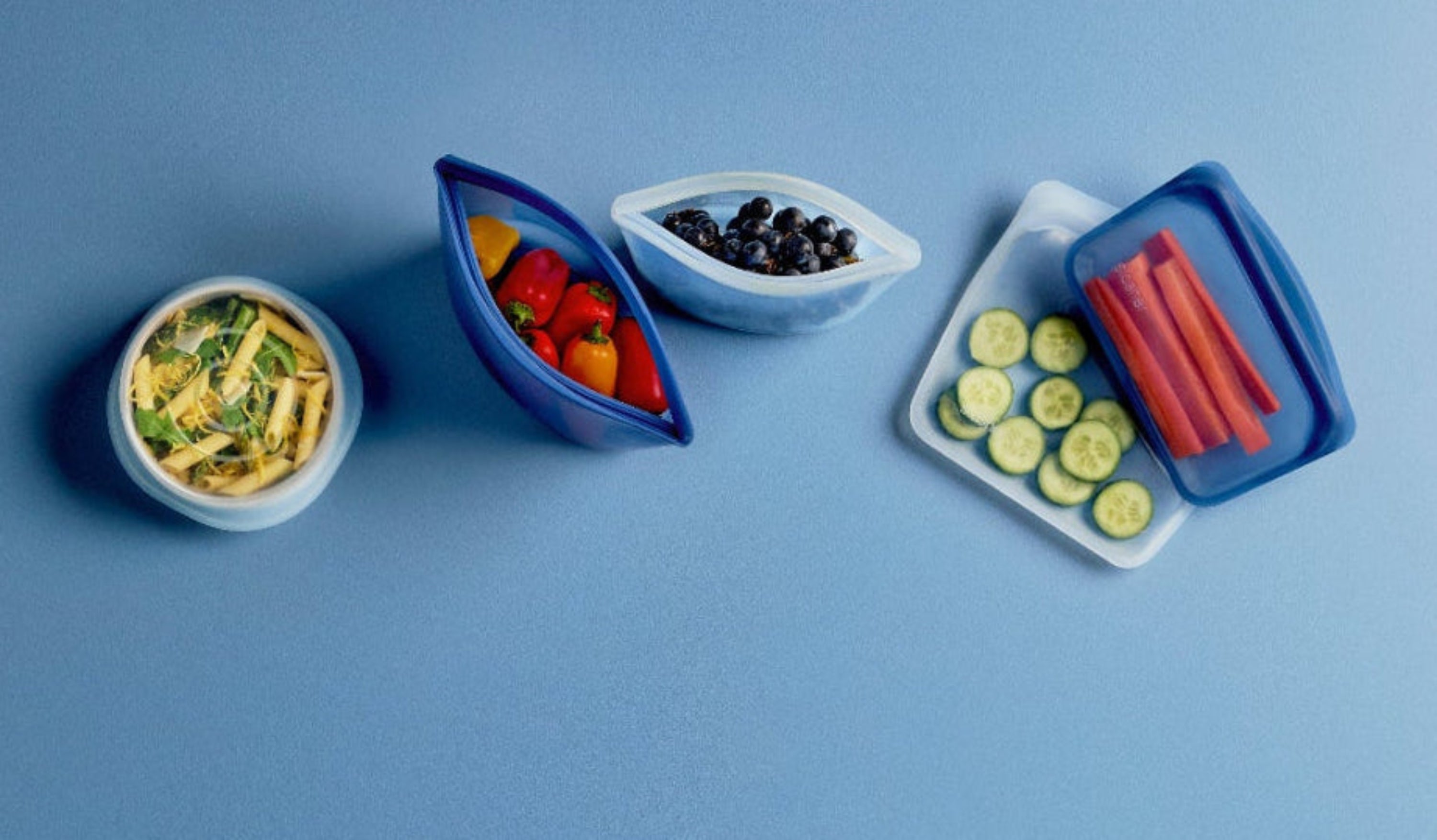 Flat lay image of stretch lids over bowls of food and bags and bowls holding various snacks. Make the switch and shop Stasher today, the gold standard for reusable bags. 