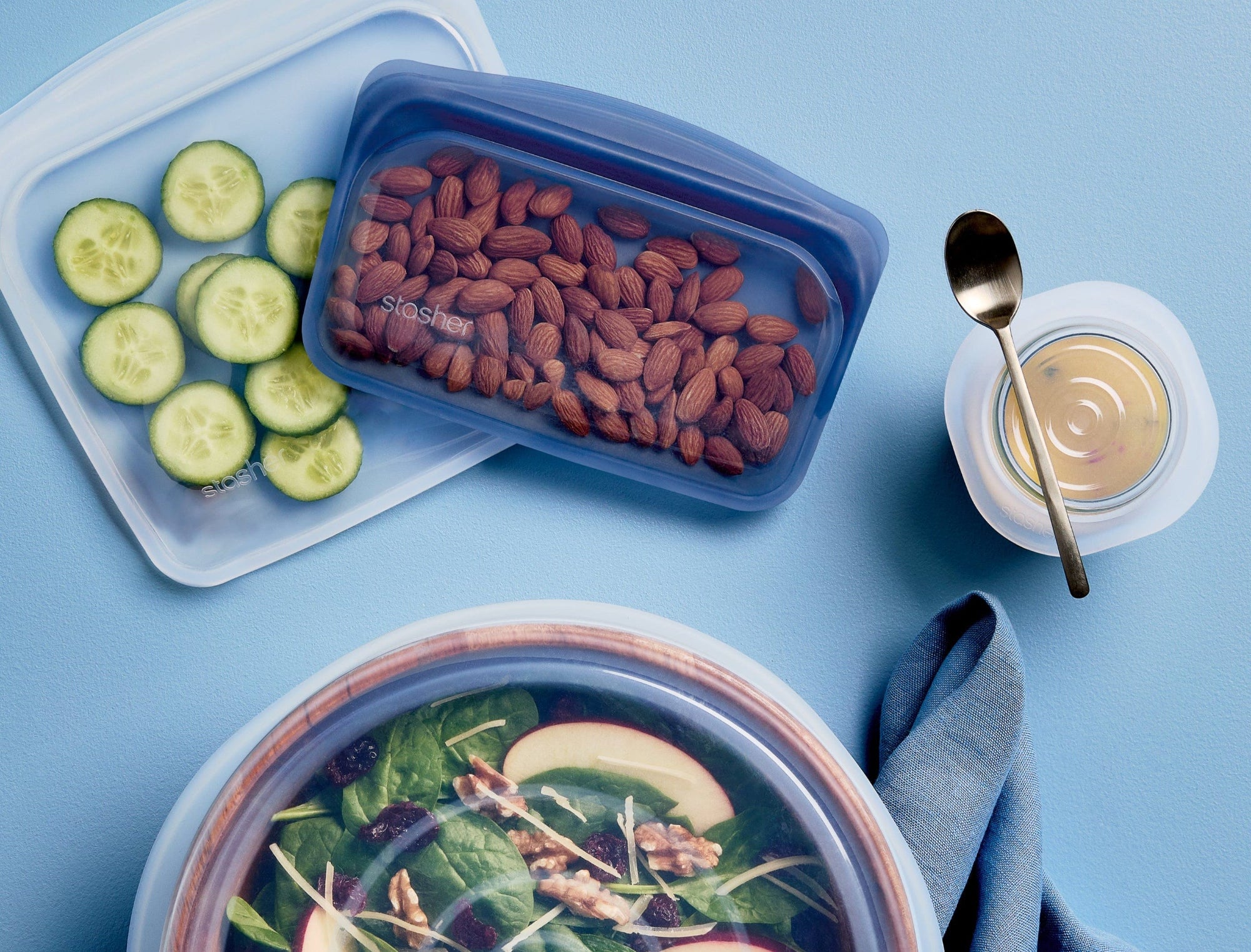Stasher sandwich and snack holding almonds and sliced cucumbers. A stretch lid covering a salad bowl. 