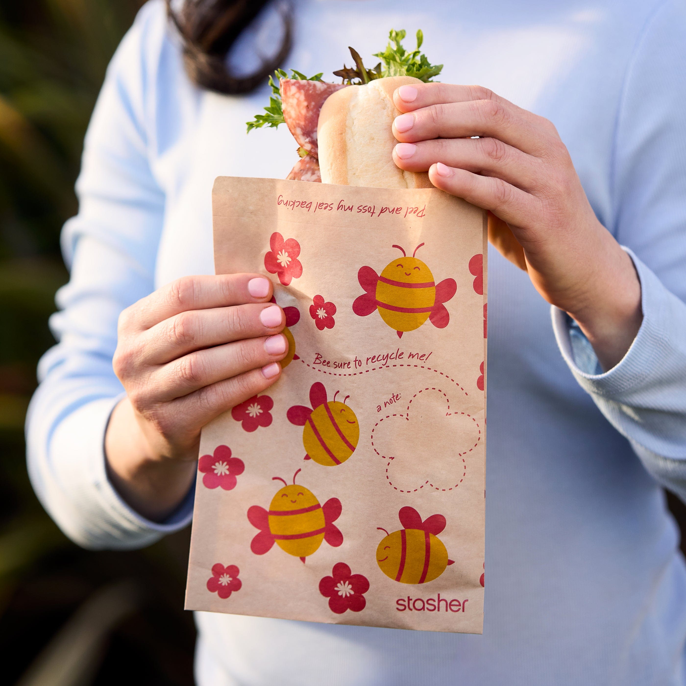 bee: paper sandwich bag held by woman with a sandwich inside.
