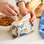 dinosaur: paper snack bag with dino prints holding twisted pretzels. 