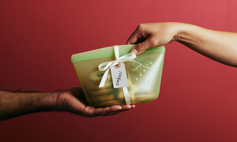 Two hands exchanging a green gift box with a white ribbon against a red background