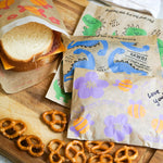 all: paper sandwich and snack bags holding a sandwich and pretzels. 