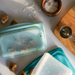 all: Three silicone food storage containers on a kitchen counter with cookie ingredients around.