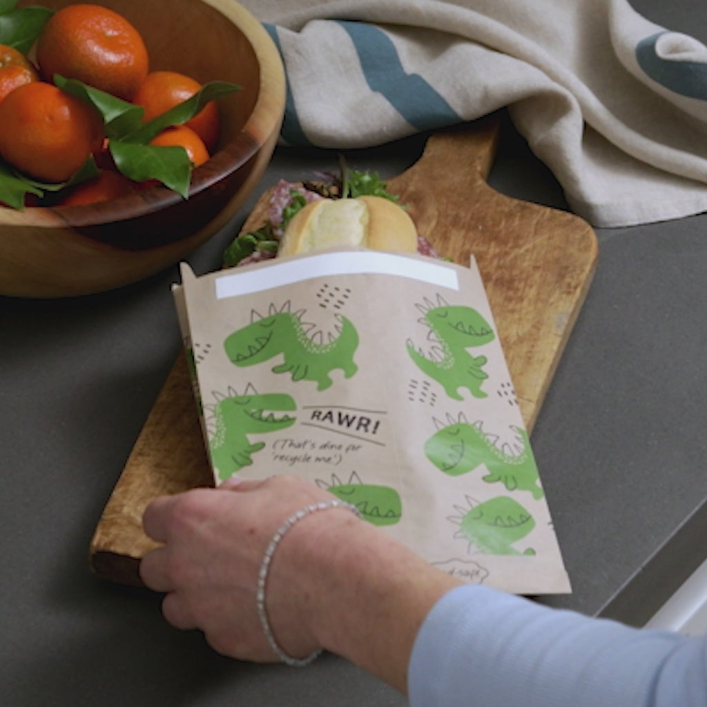 all: sandwich paper bag with dinos on it holding a sandwich.